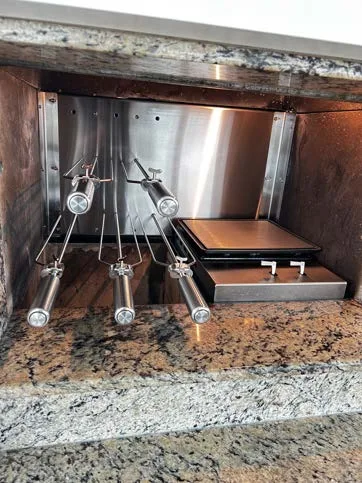 Espetos suspensos ao lado de uma bifeira, com bancada de granito